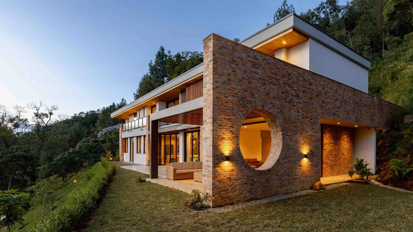 A modern brick house in the hills above Medellín, lit at dusk