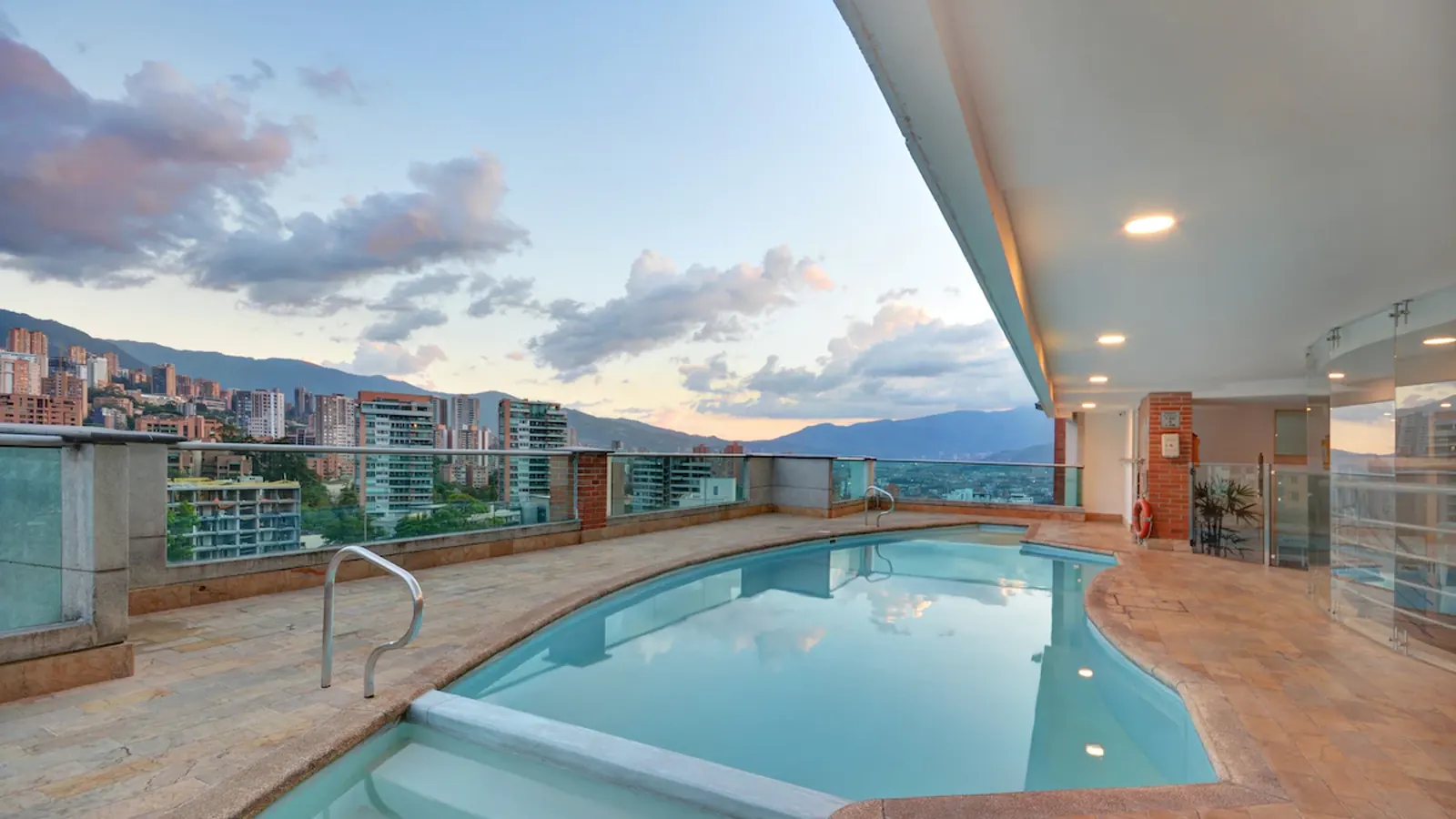 A rooftop terrace and pool at sunset, mountains on the horizon